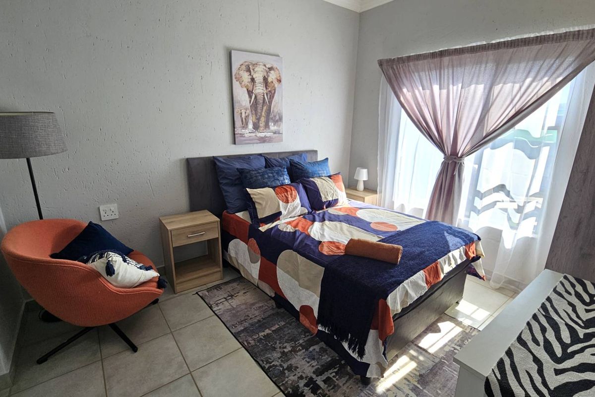 A well-lit bedroom featuring tiled flooring, neutral wall finishes, and a large window with curtain treatments.