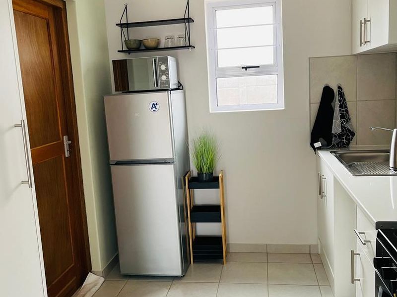 A compact, functional kitchen featuring white cabinetry, tiled flooring, and a louvered window, providing a clean and practical workspace.