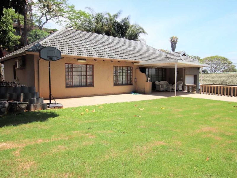 Rear view of the house featuring a tiled roof, a covered patio area, and a spacious lawn with paved sections.