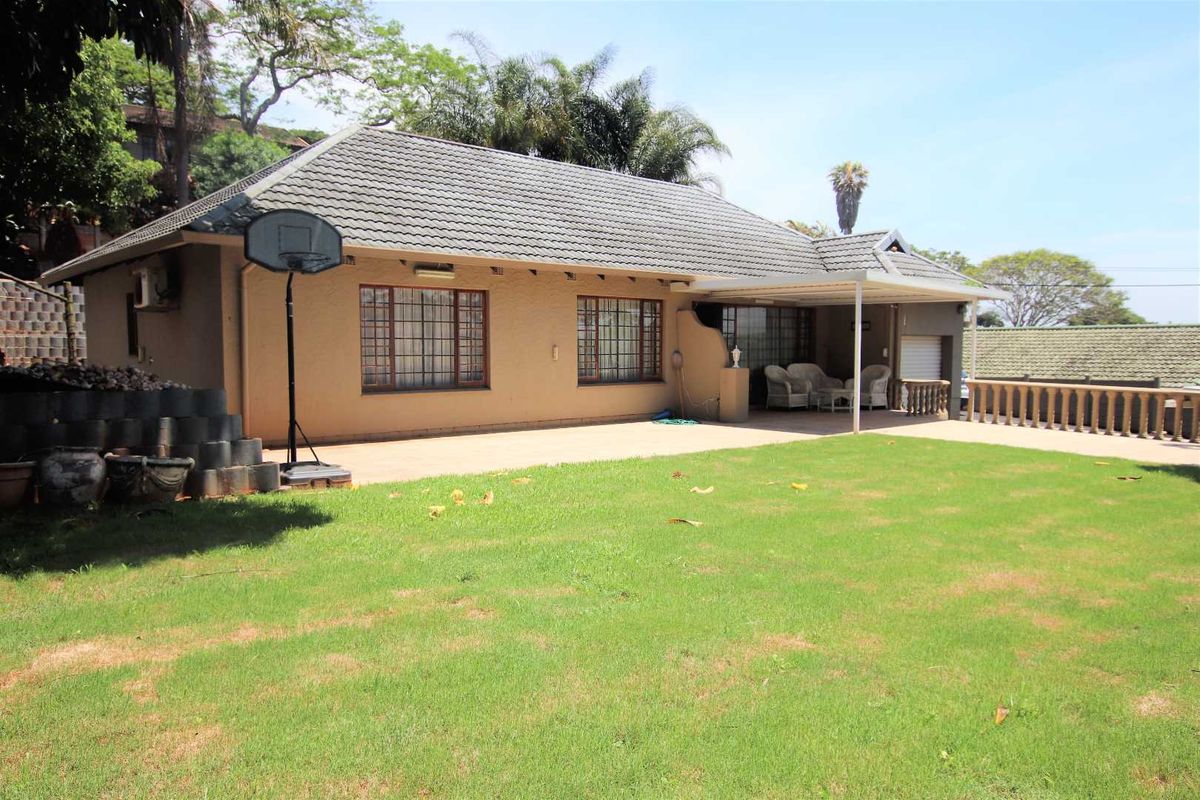 Rear view of the house featuring a tiled roof, a covered patio area, and a spacious lawn with paved sections.