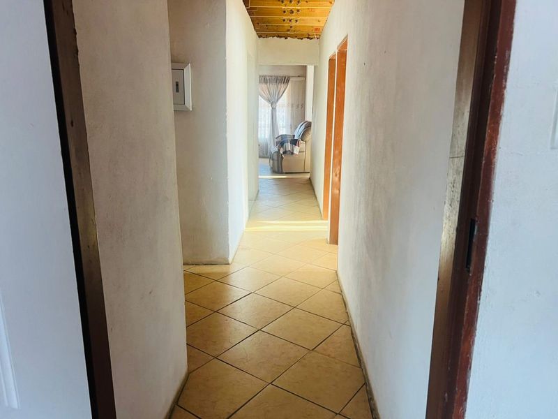 A functional hallway featuring tiled flooring and exposed timber ceiling beams, leading towards an adjacent living area.