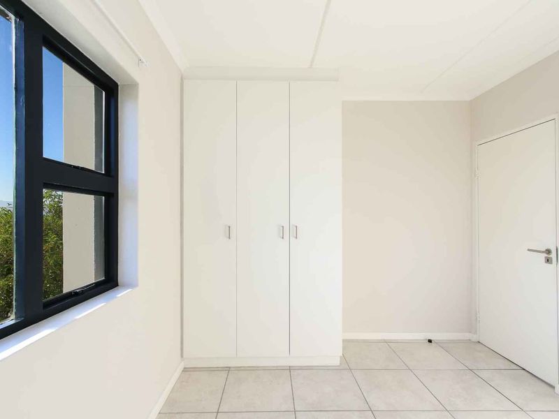A bright, empty bedroom featuring neutral tiled flooring, built-in white cupboards, and a large window with views.