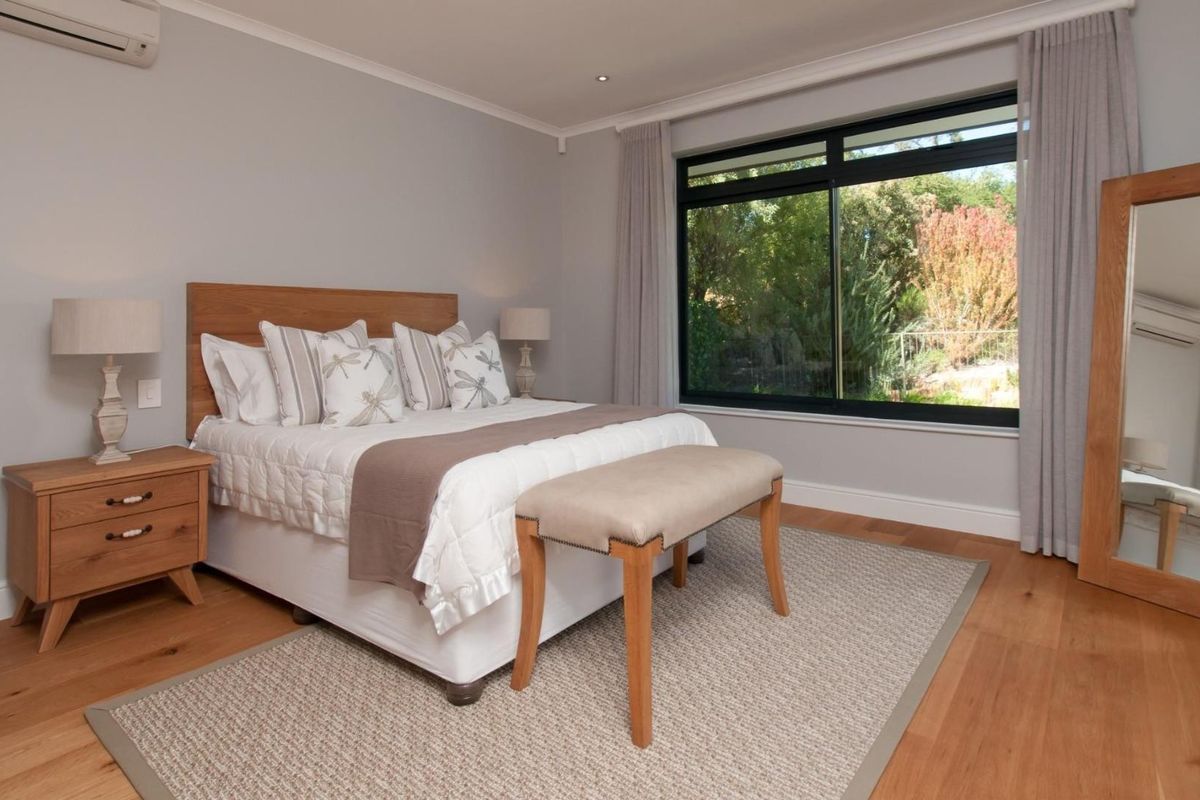 A well-maintained bedroom featuring timber flooring, a large window with garden views, and a wall-mounted air conditioning unit.