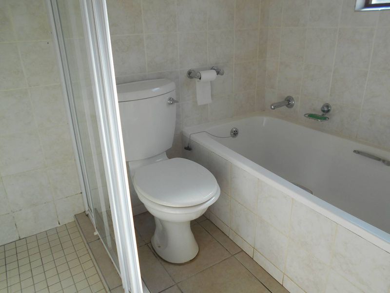 A functional bathroom featuring a built-in bathtub, separate shower enclosure, and standard toilet with neutral ceramic wall and floor tiling.