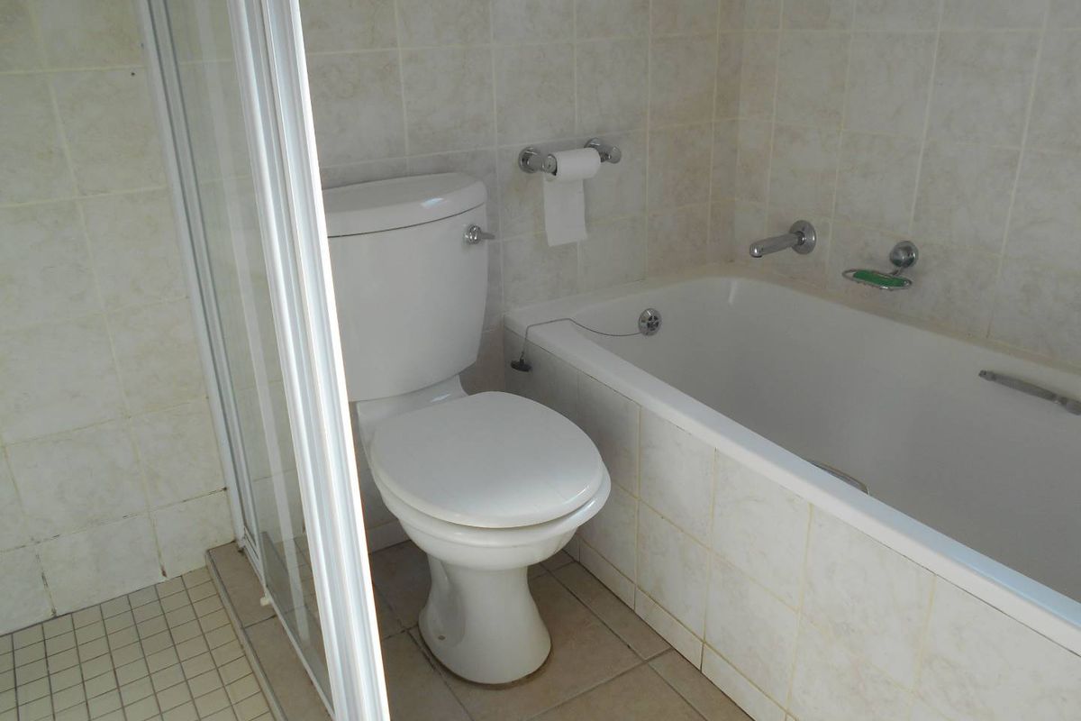 A functional bathroom featuring a built-in bathtub, separate shower enclosure, and standard toilet with neutral ceramic wall and floor tiling.