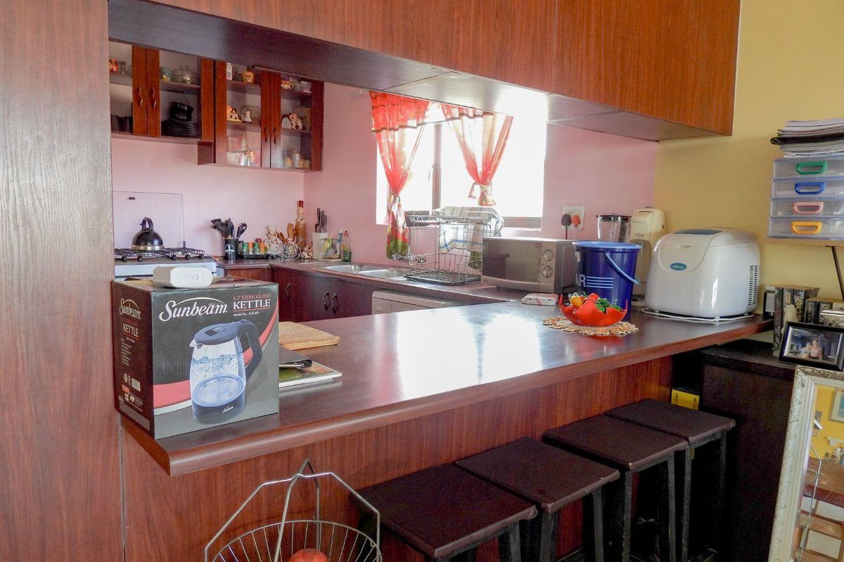 A functional kitchen featuring a breakfast bar, wooden cabinetry, and a pass-through window connecting to the adjacent living space.