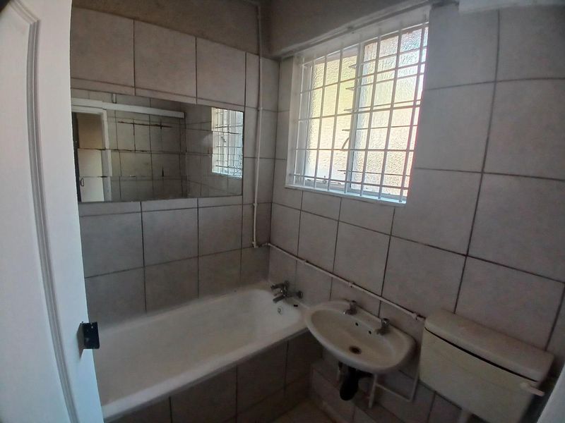 A functional bathroom featuring a bathtub, wall-mounted basin, and toilet, with tiled walls and security bars on the window.