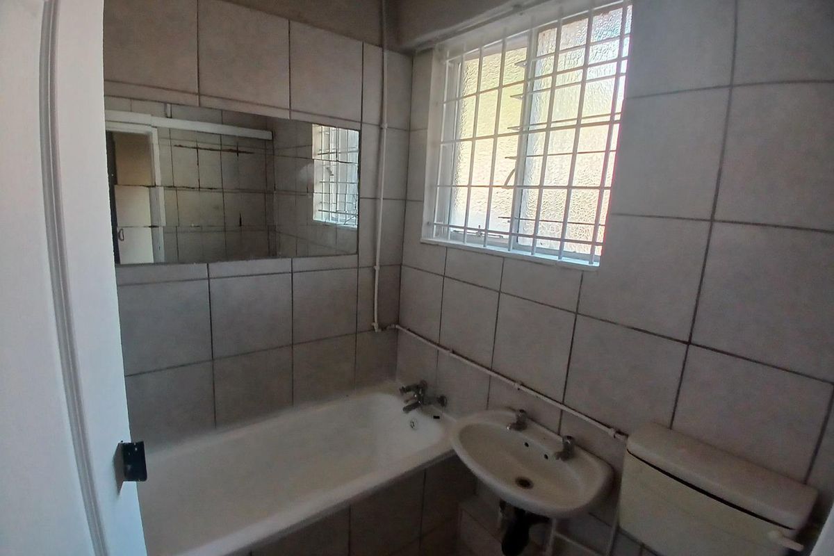A functional bathroom featuring a bathtub, wall-mounted basin, and toilet, with tiled walls and security bars on the window.