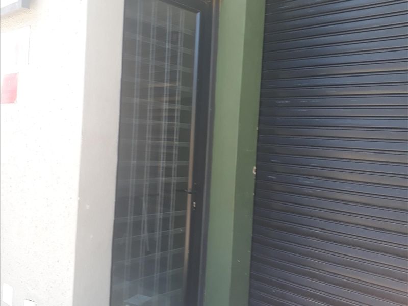 Exterior view of an industrial unit featuring a secure roller shutter door and a glass pedestrian entrance door with paved frontage.