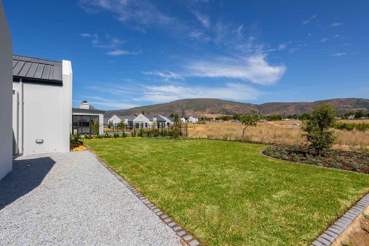 A well-maintained rear garden featuring a manicured lawn, gravel pathway, and metal fencing, offering scenic views of the surrounding landscape and mountains.