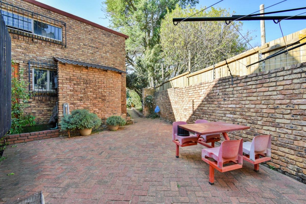 A private rear courtyard featuring brick paving, perimeter brick boundary walls, and a side pathway leading to the garden area.