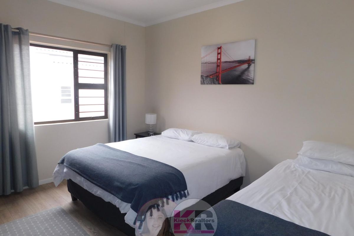 A well-maintained bedroom featuring laminate flooring and a window fitted with security bars, providing a clean and functional living space.