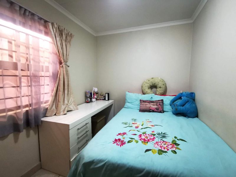 A compact bedroom featuring a built-in desk and a window fitted with security bars, providing a functional space.