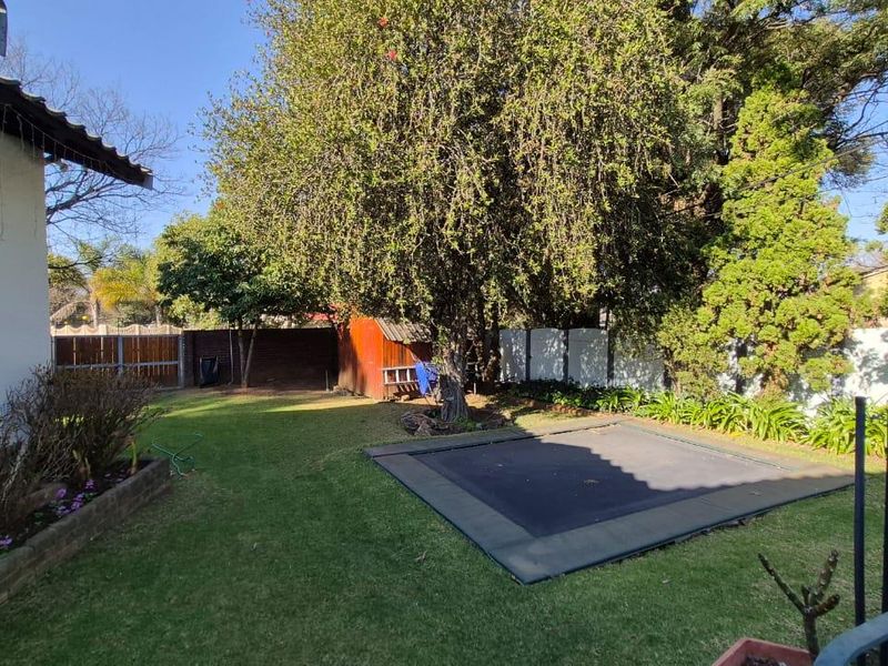 A private rear garden featuring a well-maintained lawn, mature trees, perimeter fencing, and a brick planter bed.