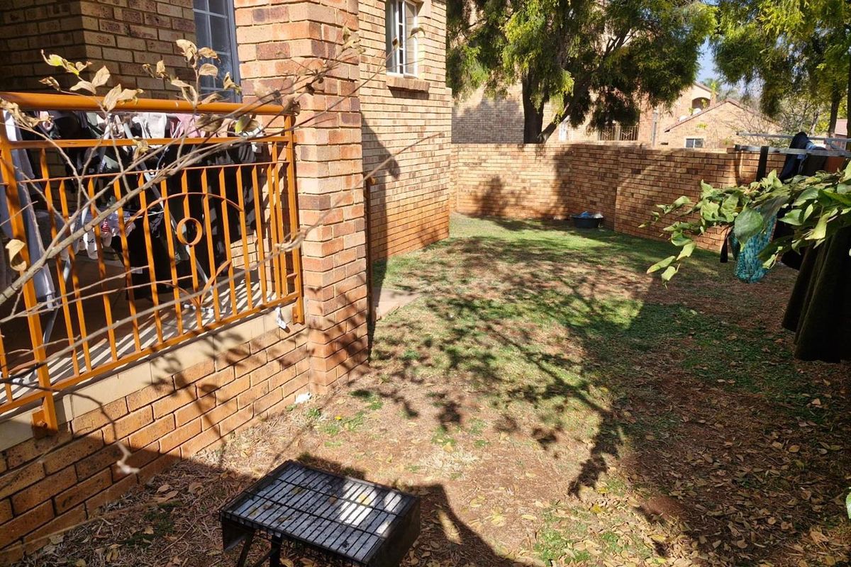 A private rear garden area featuring a brick boundary wall, a raised patio with metal railing, and established trees.