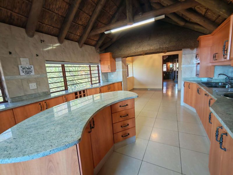 Spacious kitchen featuring granite countertops, extensive wooden cabinetry, and a unique vaulted thatched ceiling with exposed timber beams.