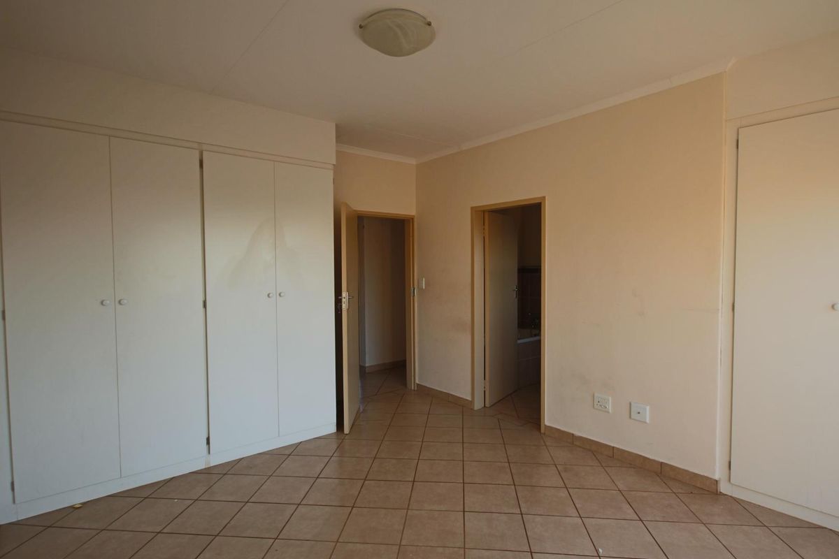 A vacant bedroom featuring built-in cupboards, tiled flooring, and direct access to an adjoining bathroom.