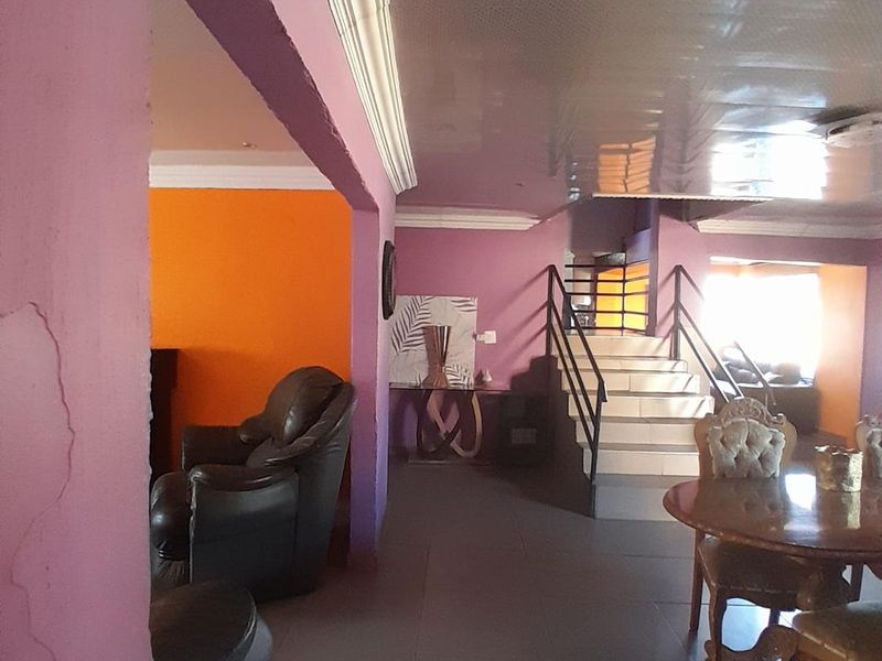 Open plan living area featuring a central staircase with metal balustrades, tiled flooring, and distinctive purple and orange wall finishes.