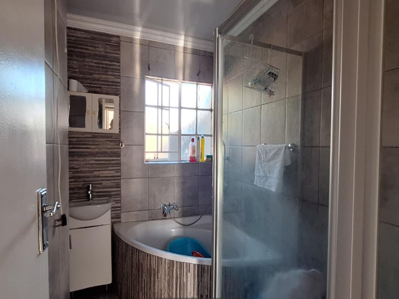 A functional bathroom featuring a corner bathtub, separate shower enclosure, and a vanity basin with tiled wall finishes.