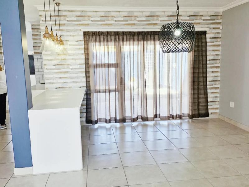 Open plan living and kitchen area featuring tiled flooring, a central kitchen island, pendant lighting, and a sliding glass door leading to the exterior.