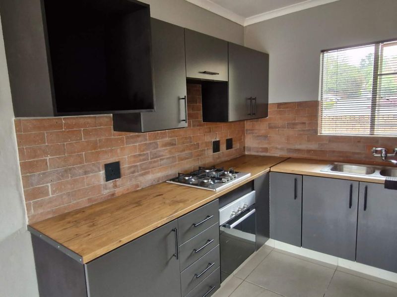 Modern kitchen featuring dark grey cabinetry, wooden countertops, a gas hob, built-in oven, and a stylish brick-style tiled backsplash.