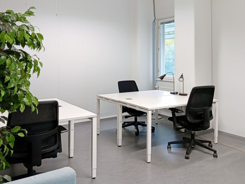 A bright, functional office space featuring clean white walls, neutral flooring, and a window providing natural light.