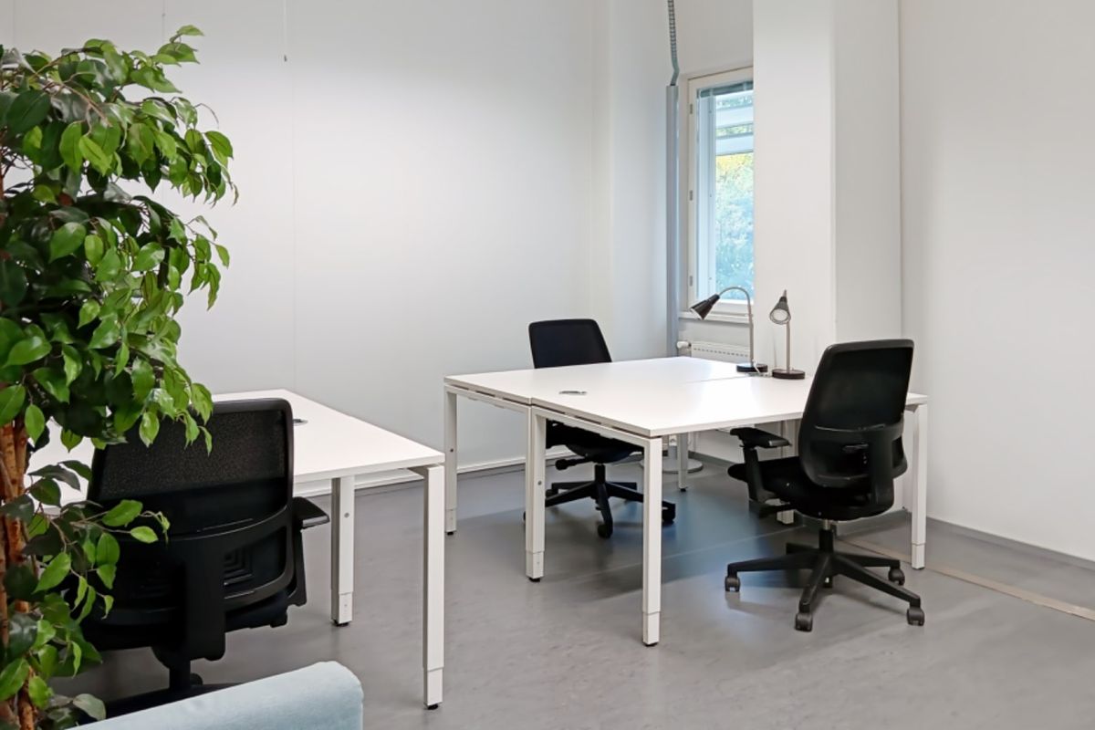 A bright, functional office space featuring clean white walls, neutral flooring, and a window providing natural light.