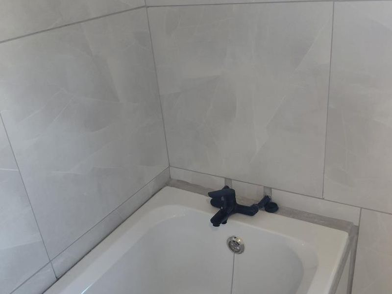 A clean bathroom featuring a built-in bathtub with modern black fixtures and neutral wall tiling.