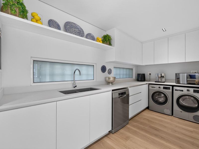 Modern, well-appointed laundry room featuring sleek white cabinetry, stone countertops, integrated sink, and dedicated space for laundry appliances.
