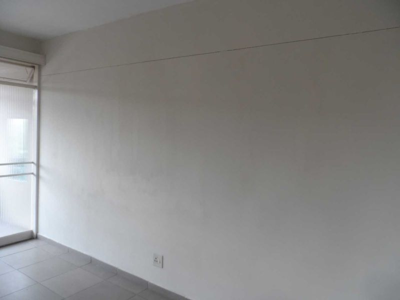 An empty living room featuring tiled flooring and a sliding glass door, showing signs of wall surface wear and a horizontal crack.