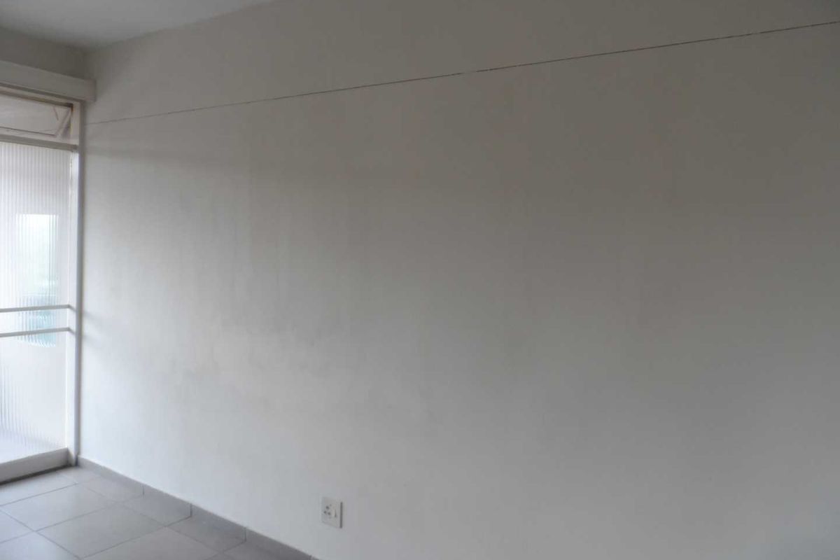 An empty living room featuring tiled flooring and a sliding glass door, showing signs of wall surface wear and a horizontal crack.