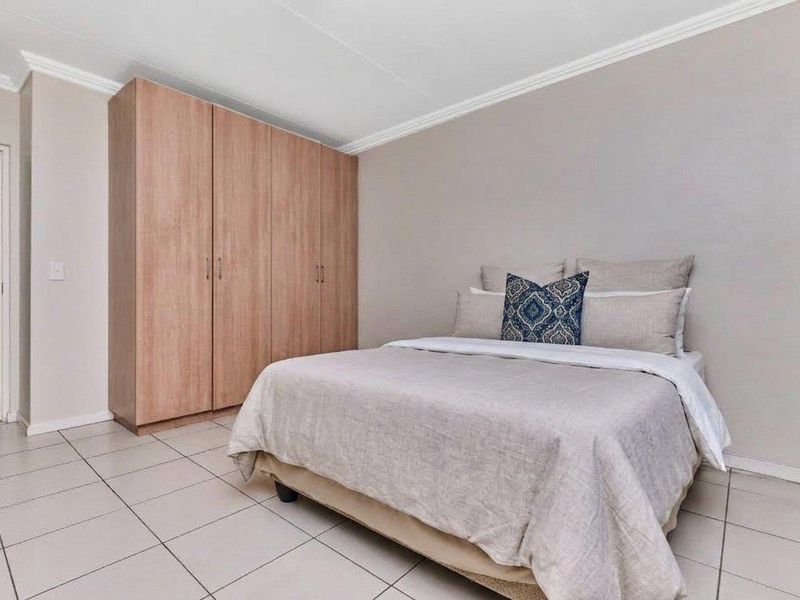A well-maintained bedroom featuring neutral wall tones, tiled flooring, crown molding, and a spacious built-in wardrobe.