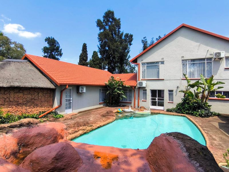 Rear exterior view featuring a swimming pool with natural rock surrounds, a thatched roof section, and multi-level building facade.