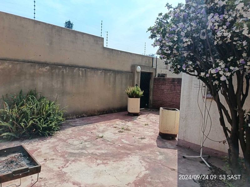A private rear courtyard featuring paved flooring, perimeter walls with electric fencing, and established garden elements, offering potential for outdoor living enhancement.