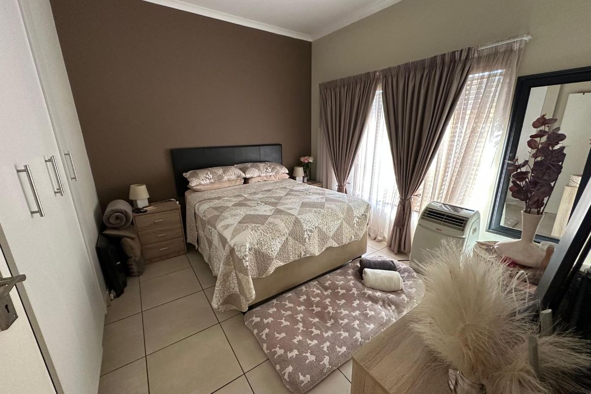 A well-lit bedroom featuring neutral tiled flooring, built-in cupboards, and a feature wall, offering a comfortable and functional living space.