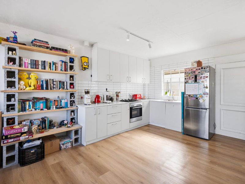 A bright kitchen featuring white cabinetry, subway tile backsplash, built-in oven, gas hob, and modern laminate flooring.