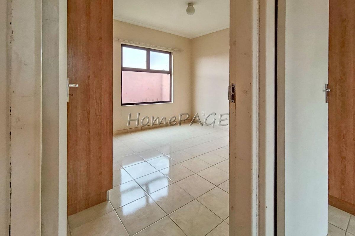 A view into an empty bedroom featuring tiled flooring and a window, viewed through a doorway.