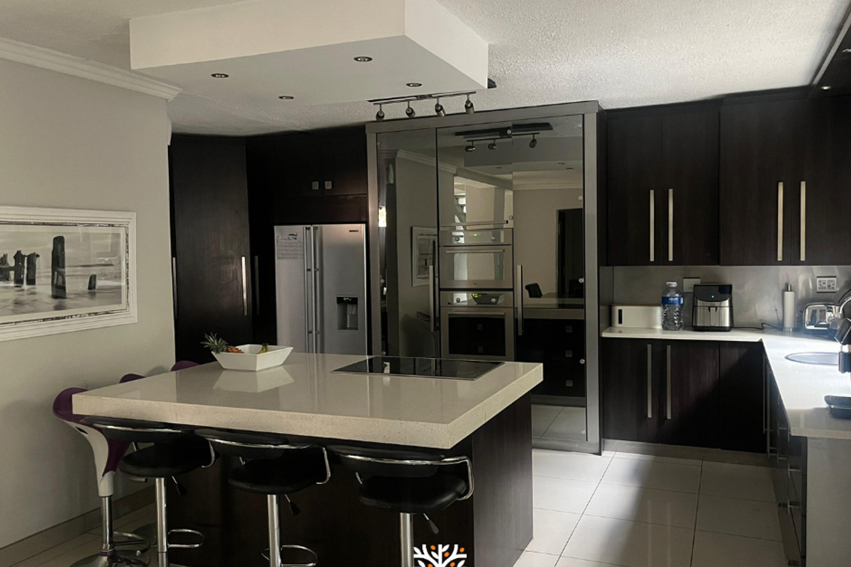 Modern kitchen featuring dark wood cabinetry, a large central island with quartz countertops, built-in appliances, and recessed lighting.