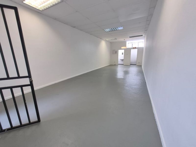 An open-plan retail space featuring a painted concrete floor, suspended ceiling with recessed lighting, and a secure entrance gate.