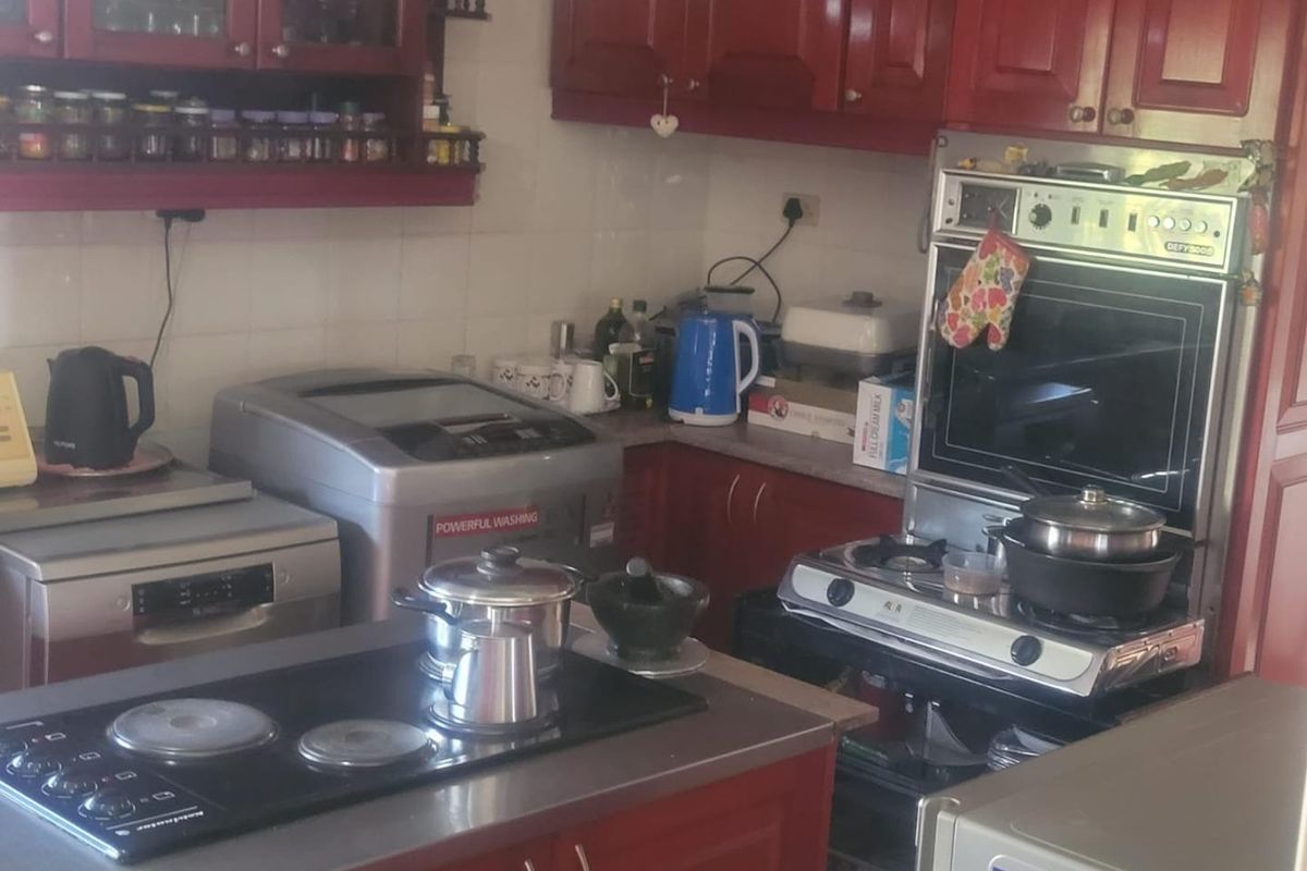 A functional kitchen featuring red cabinetry, built-in oven, hob, and extractor fan with tiled splashbacks and ample counter space.