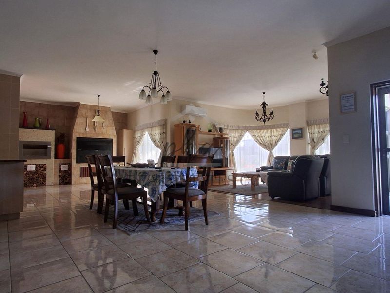 Spacious open-plan living and dining area featuring tiled flooring, a built-in fireplace, and a built-in braai, offering a versatile layout for family living.
