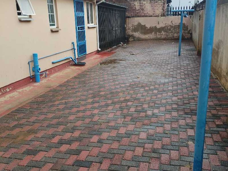 A paved rear courtyard area featuring a boundary wall and direct access to the house via a security gate.