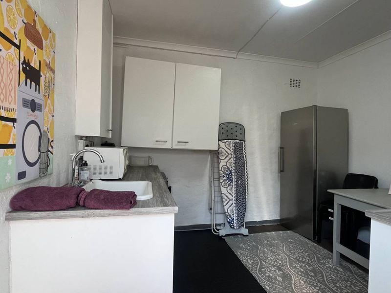A functional laundry area featuring built-in white cabinetry, a laminate countertop, and a sink, providing practical utility space within the cottage.