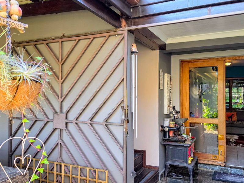 A covered entrance area featuring a decorative metal security gate, timber-framed glass door, and stone flooring, providing a welcoming transition into the home.