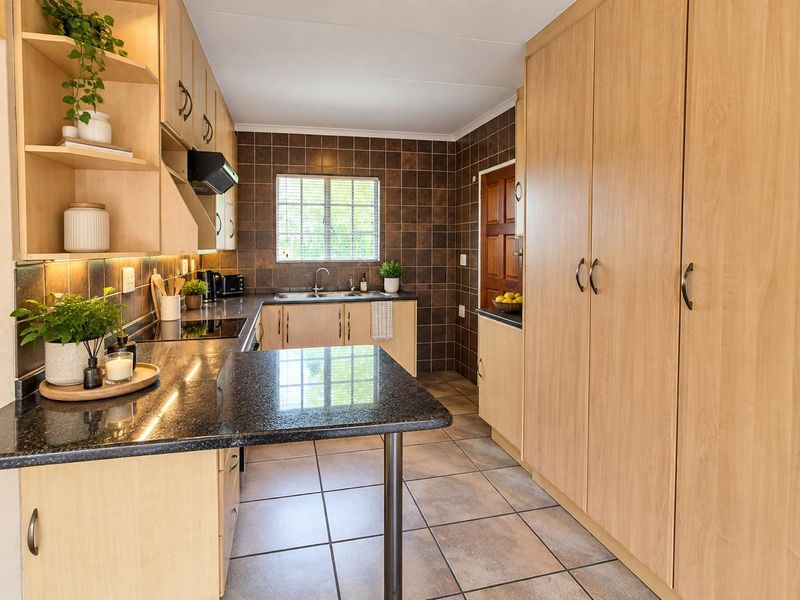 A well-maintained kitchen featuring light wood cabinetry, dark granite countertops, tiled backsplash, and ample storage space with a full-height pantry cupboard.