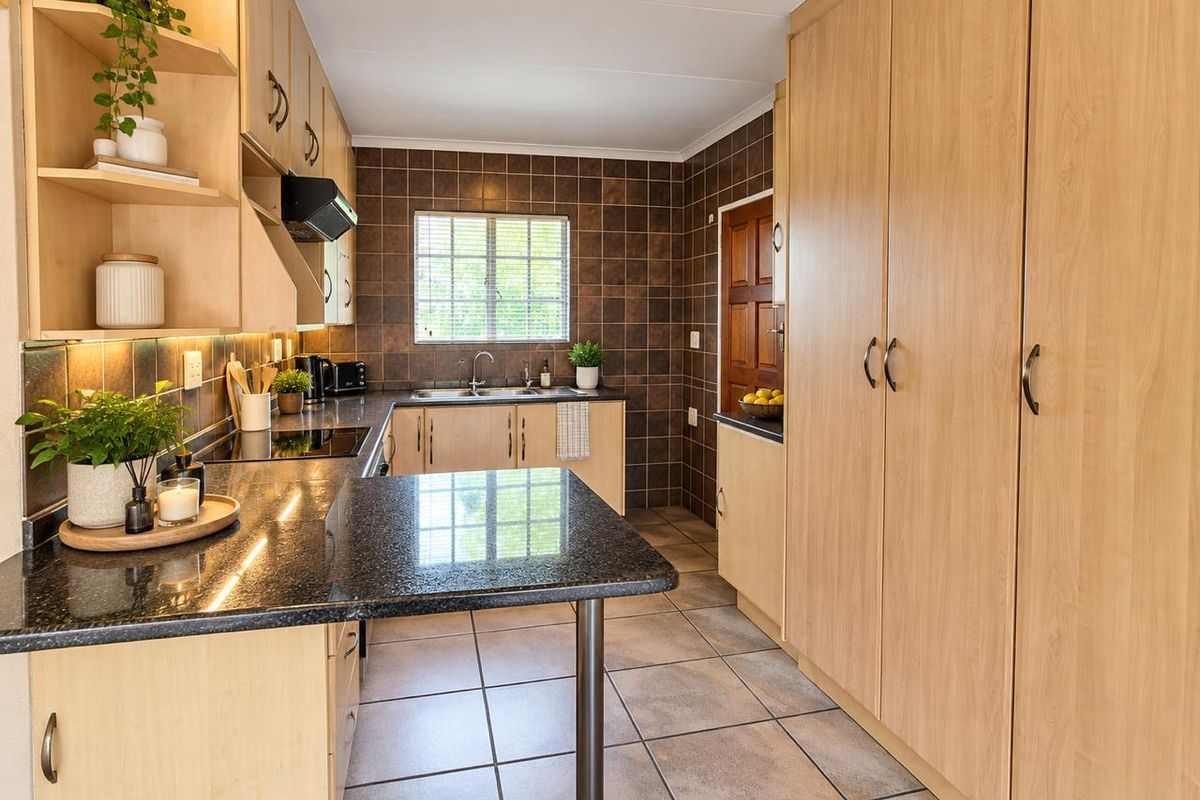 A well-maintained kitchen featuring light wood cabinetry, dark granite countertops, tiled backsplash, and ample storage space with a full-height pantry cupboard.