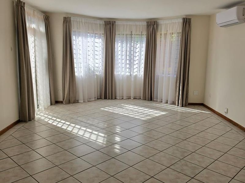 Spacious, light-filled living area featuring neutral ceramic tile flooring, a large bay window, and a wall-mounted split-system air conditioner.