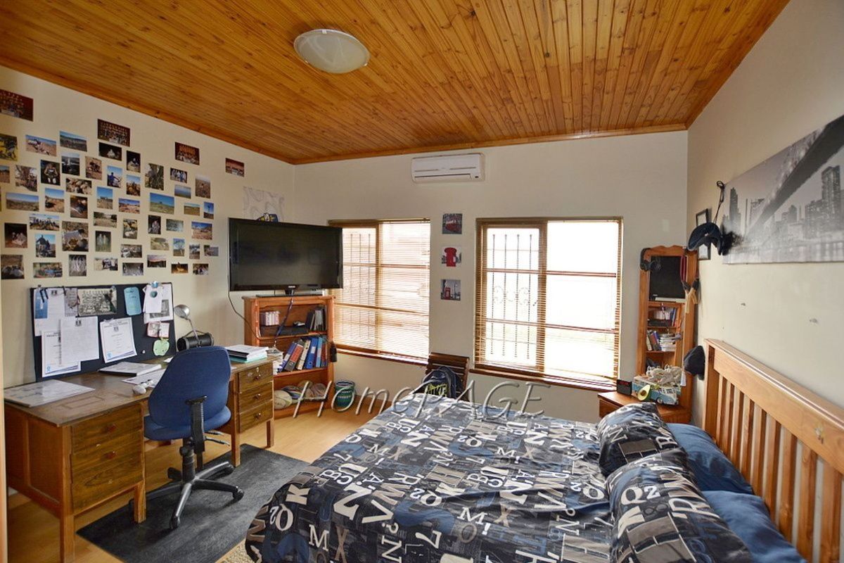 A bedroom featuring a timber-clad ceiling, split-system air conditioning unit, and large windows with security bars.