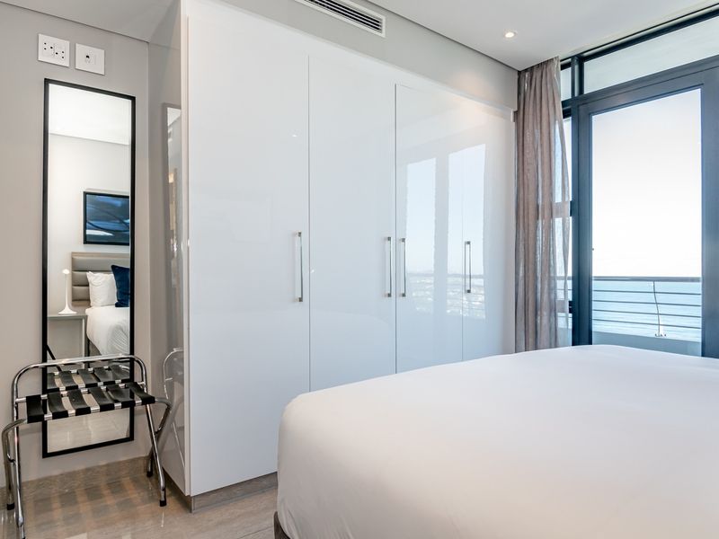 Modern bedroom featuring high-gloss built-in cupboards, ducted air conditioning, and large sliding glass doors opening to a balcony with ocean views.