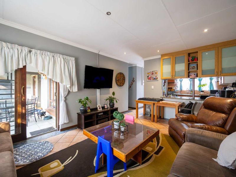 Open-plan living area featuring tiled floors, recessed lighting, and a kitchen pass-through window, with direct access to an outdoor patio area.